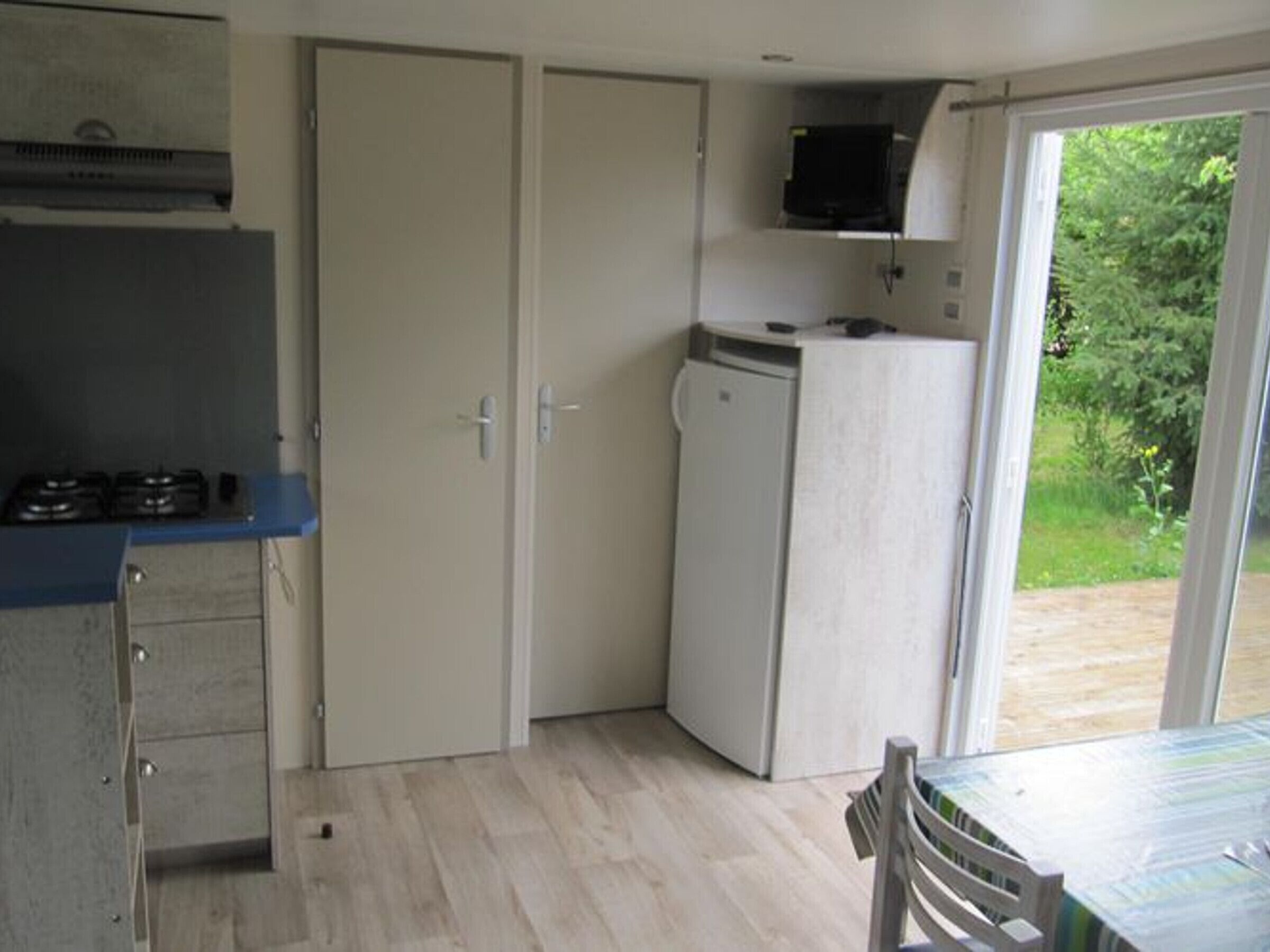 A compact kitchen with a gas stove, a microwave, and a refrigerator. There is a dining table with chairs and a sliding glass door leading to an outdoor area.