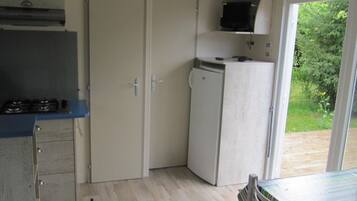 A compact kitchen with a gas stove, a microwave, and a refrigerator. There is a dining table with chairs and a sliding glass door leading to an outdoor area.