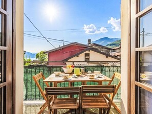 Un balcón abierto con una mesa dispuesta para el té, sillas de madera y vistas a un edificio rojo y montañas.