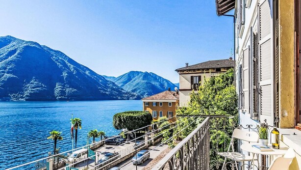 A balcony with a view of a lake and mountains, a parked car, and a building with a balcony. - Nice apartment for 4 guests with WIFI, balcony and pets allowed (Argegno)
