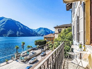 Un balcon donnant sur un lac et des montagnes, une voiture garée et un immeuble doté d’un balcon.
