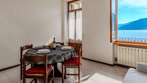 A dining area with a table set for two, a window with a view of a lake and mountains, and a radiator on the wall. - Nice apartment for 4 guests with WIFI, balcony and pets allowed (Argegno)