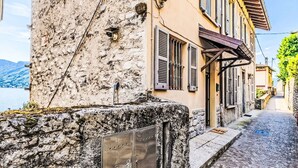 A narrow cobblestone street with a building featuring a stone facade and shuttered windows. - Nice apartment for 4 guests with WIFI, balcony and pets allowed (Argegno)
