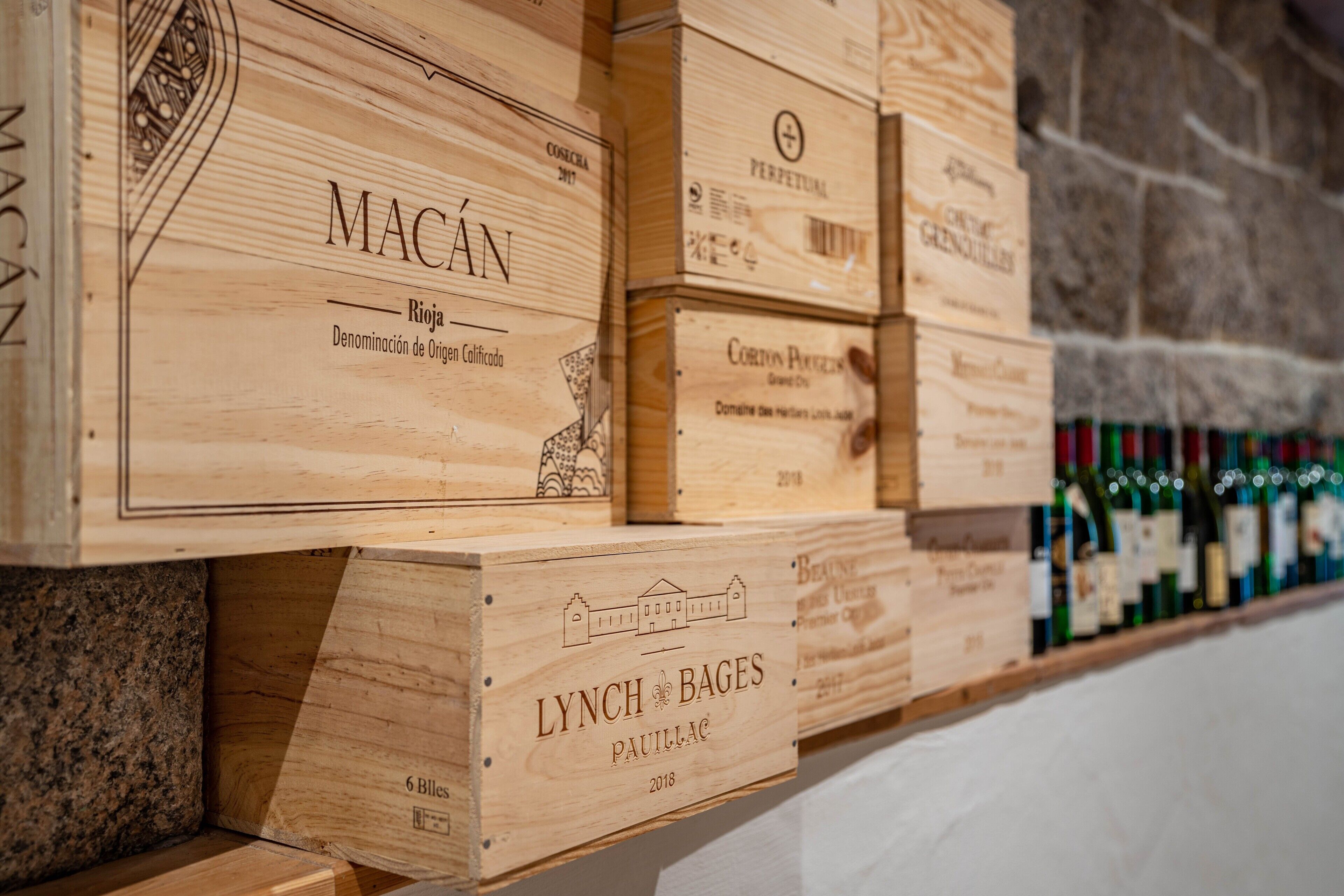 Cajas de madera para guardar vino, con etiquetas, apiladas contra una pared de piedra.