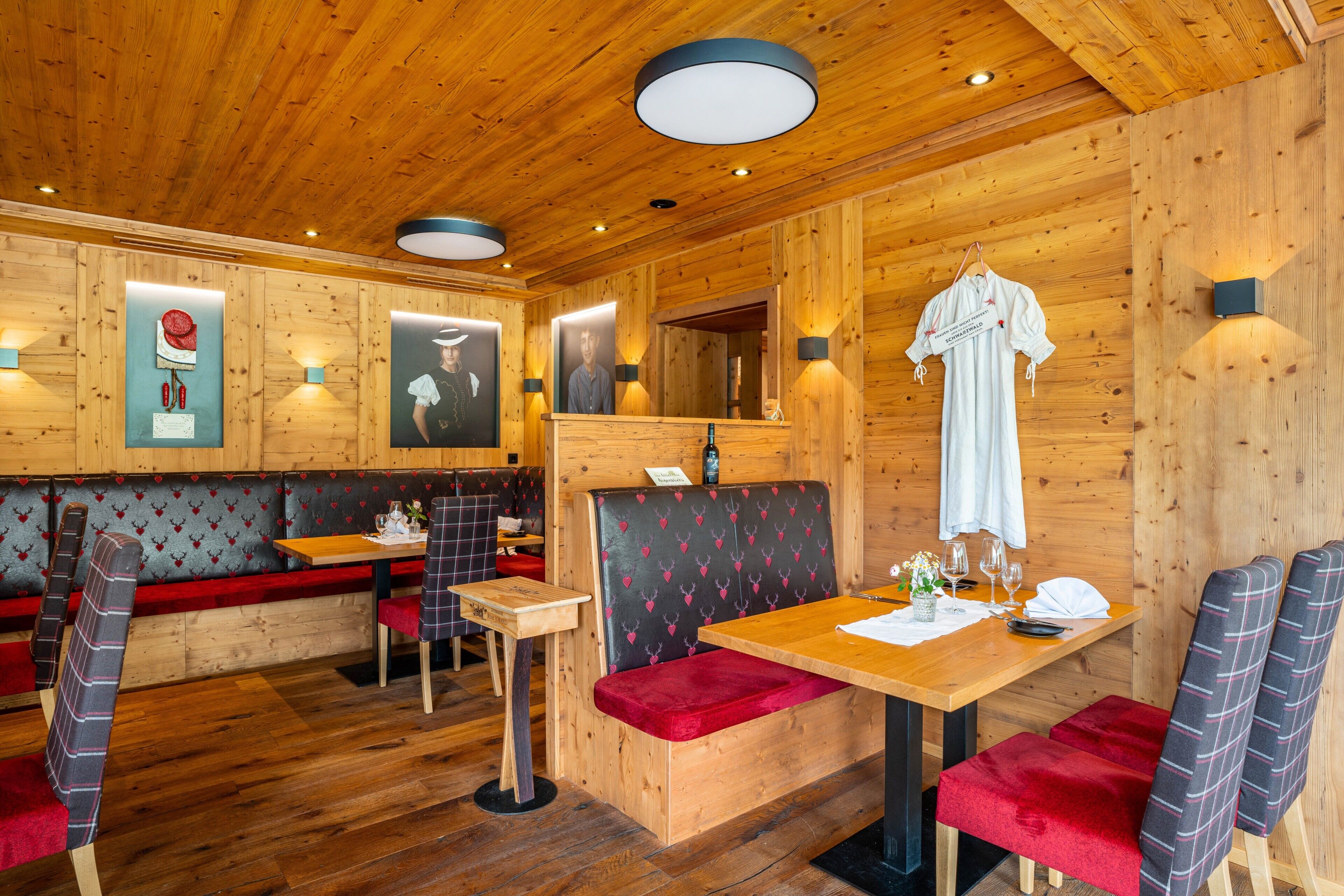 A wooden interior with a wooden ceiling, a table with a red bench, and a wall-mounted light fixture.