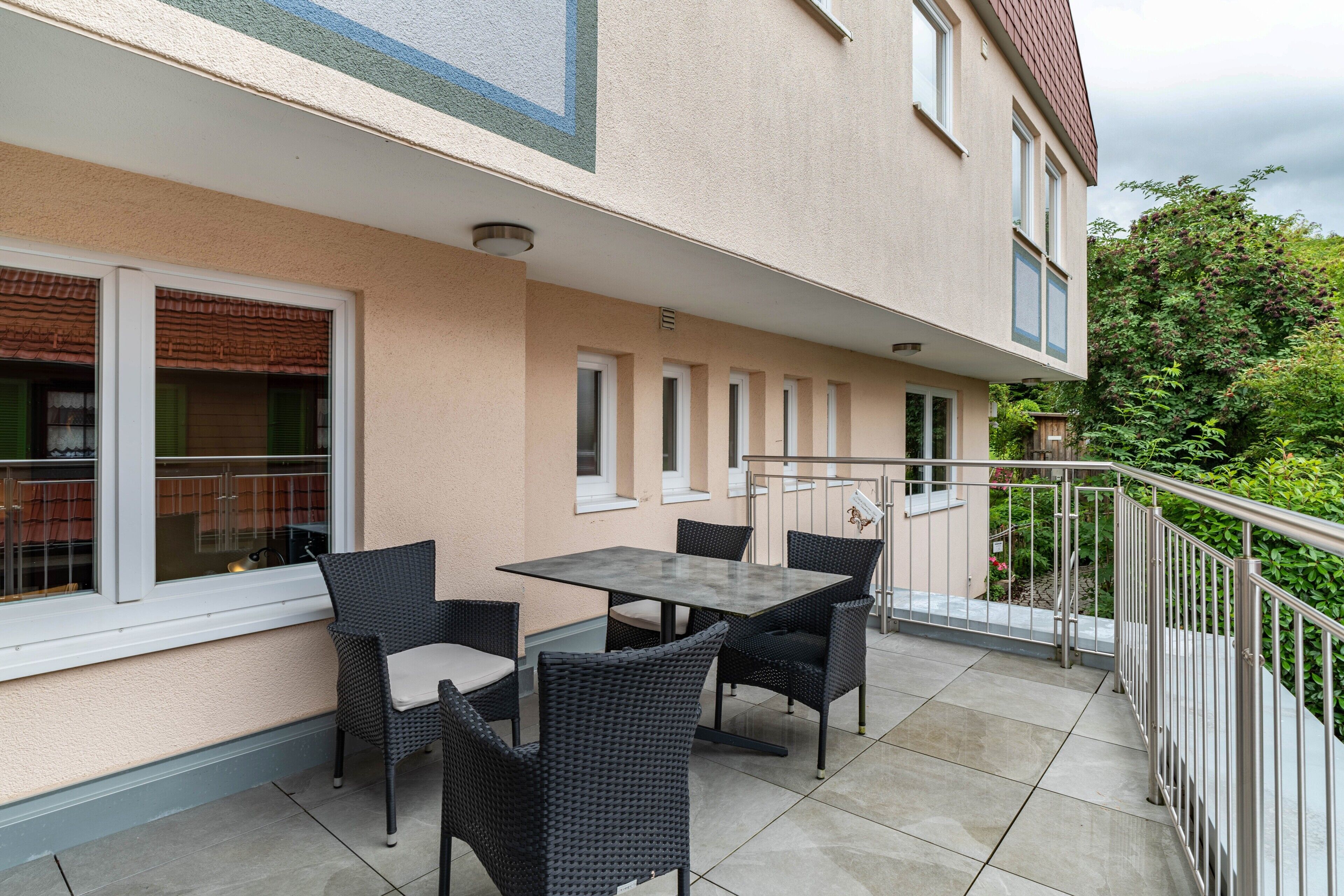 An outdoor patio with a table and chairs, a railing, and a view of a building with windows.