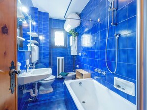 A bathroom with blue tiles, a white bathtub, a white sink, and a toilet.