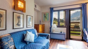 Una sala de estar con un sofá azul, un mueble de madera y un ventanal con vistas a un paisaje montañoso.