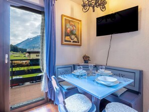 A dining area with a table set for four, a television mounted on the wall, and a painting above the table.