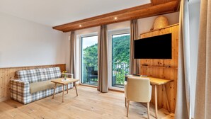 Ein modernes Zimmer mit Holzboden, einer Couch, einem Tisch, einem Stuhl und einem an einer Holzwand montierten Fernseher.