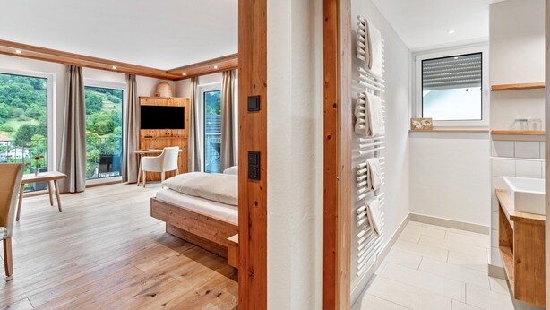 Ein modernes Schlafzimmer mit Holzboden, einem Bett, einem Fernseher und einem großen Fenster mit Blick auf Grünflächen.
