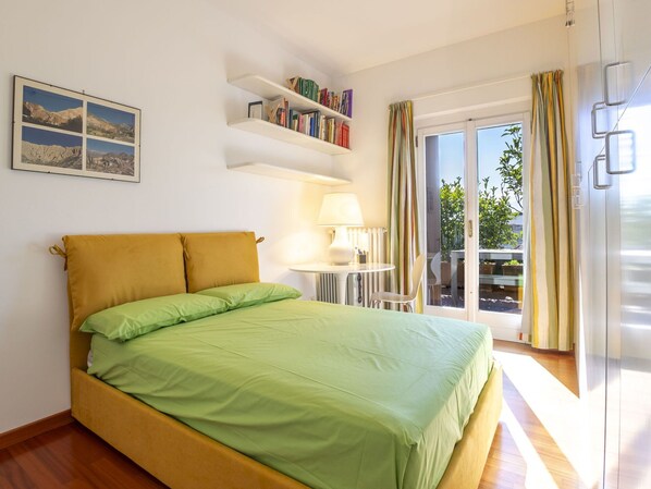 A bedroom with a bed, a bookshelf, a lamp, and a view of the outdoors.