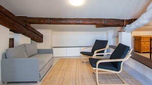 A cozy room with a grey sofa, two black chairs, a woven rug, and exposed wooden beams. - Nice apartment for 2 people with WIFI, A/C, TV, terrace and pets allowed (Pisa)
