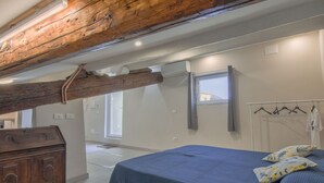 A bedroom with a wooden ceiling beam, a bed with a blue checkered bedspread, a wooden dresser, and a window with curtains. - Nice apartment for 2 people with WIFI, A/C, TV, terrace and pets allowed (Pisa)