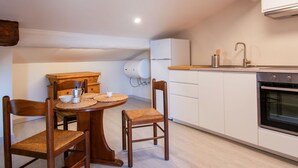 A compact kitchen with a dining area, featuring a round wooden table, two chairs, a white refrigerator, a sink, and a built-in oven. - Nice apartment for 2 people with WIFI, A/C, TV, terrace and pets allowed (Pisa)