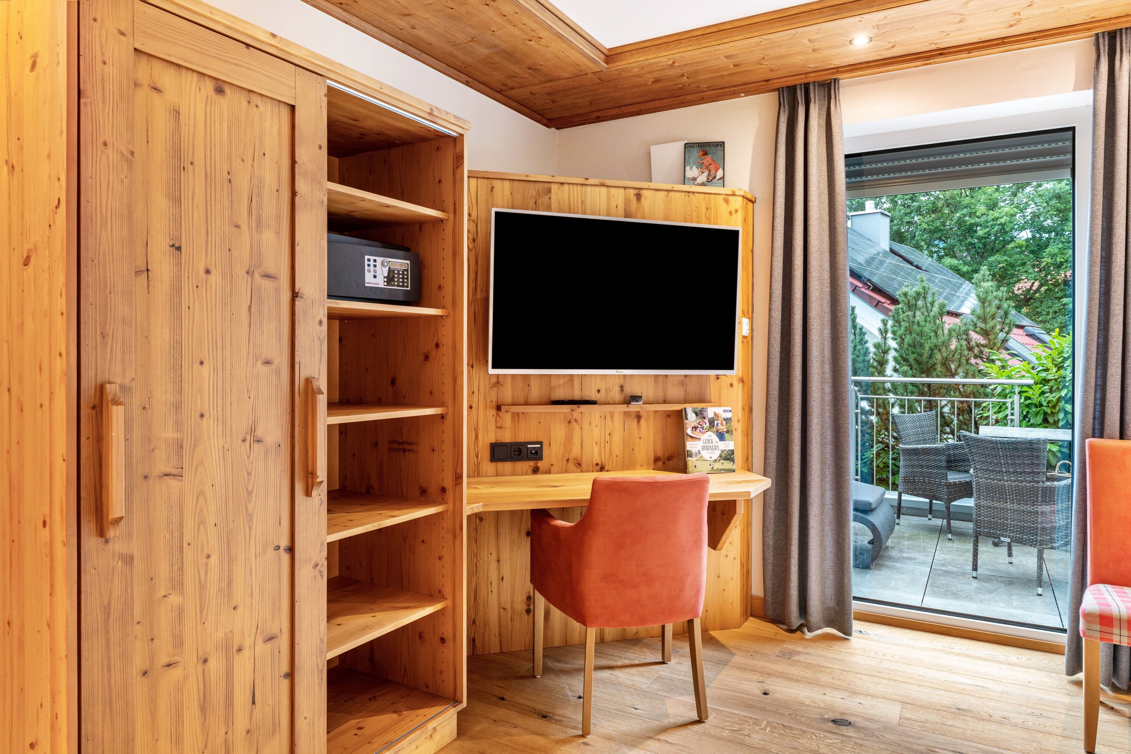 Ein Zimmer mit einem Holztisch, einem Fernseher und Blick auf einen Außenbalkon mit Möbeln.