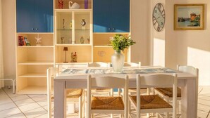 A dining area with a white table and chairs, a blue cabinet with glass doors, and a clock on the wall. - Beautiful apartment for 6 people with terrace and pets allowed (Stintino)