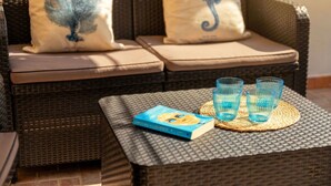 A wicker sofa with cushions, a woven table with a book and glasses, and a patterned wall. - Beautiful apartment for 6 people with terrace and pets allowed (Stintino)
