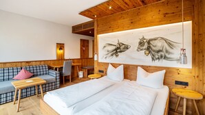 A hotel room with a bed, a sofa, a desk, and a painting of cows.