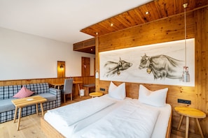 A hotel room with a bed, a sofa, a desk, and a painting of cows.