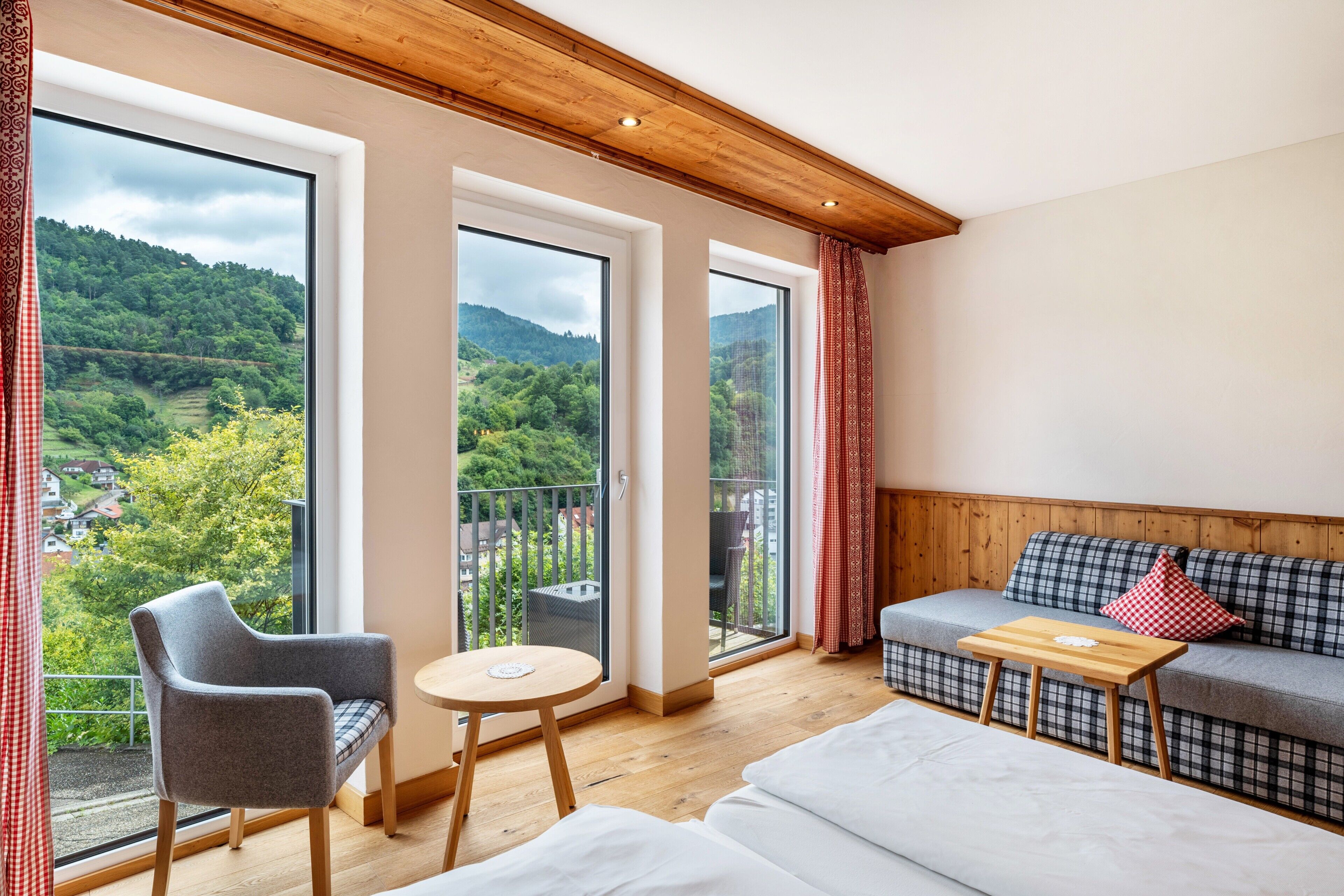 Habitación con sofá, una silla, una mesita y amplios ventanales con vistas a un paisaje verde.