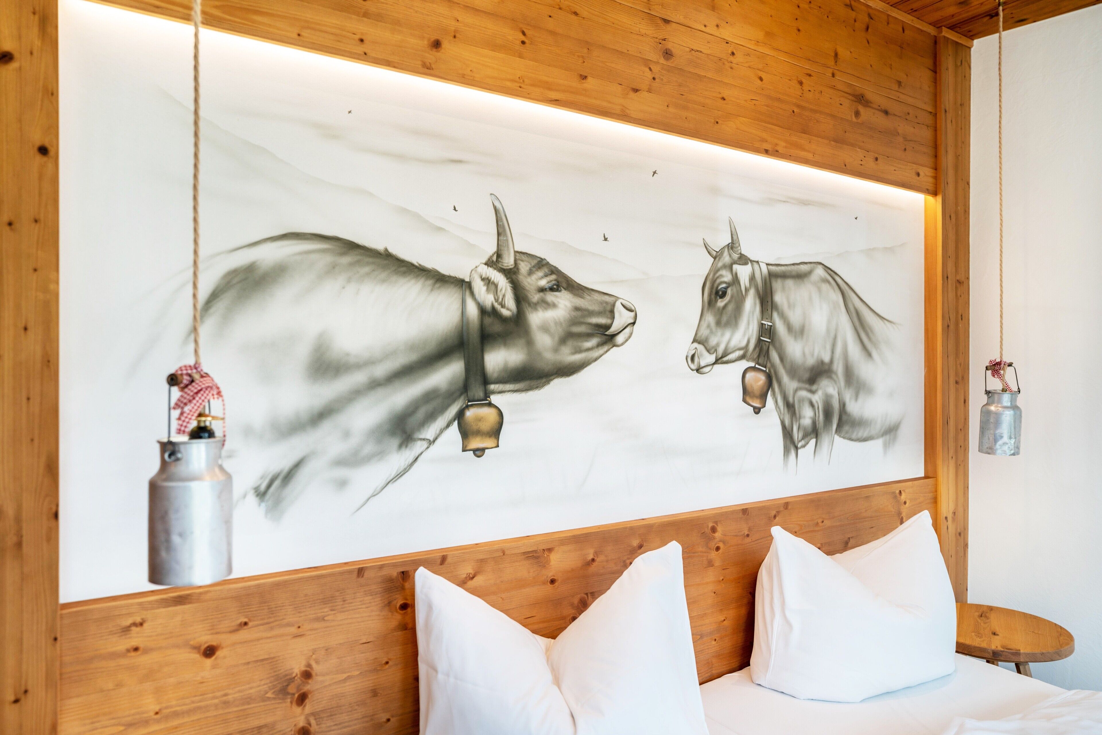 Una habitación con cabecera de madera, cama con ropa blanca y un mural en la pared con dos vacas.
