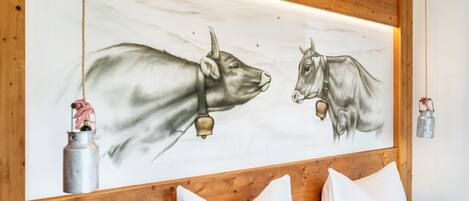 Una habitación con cabecera de madera, cama con ropa blanca y un mural en la pared con dos vacas.