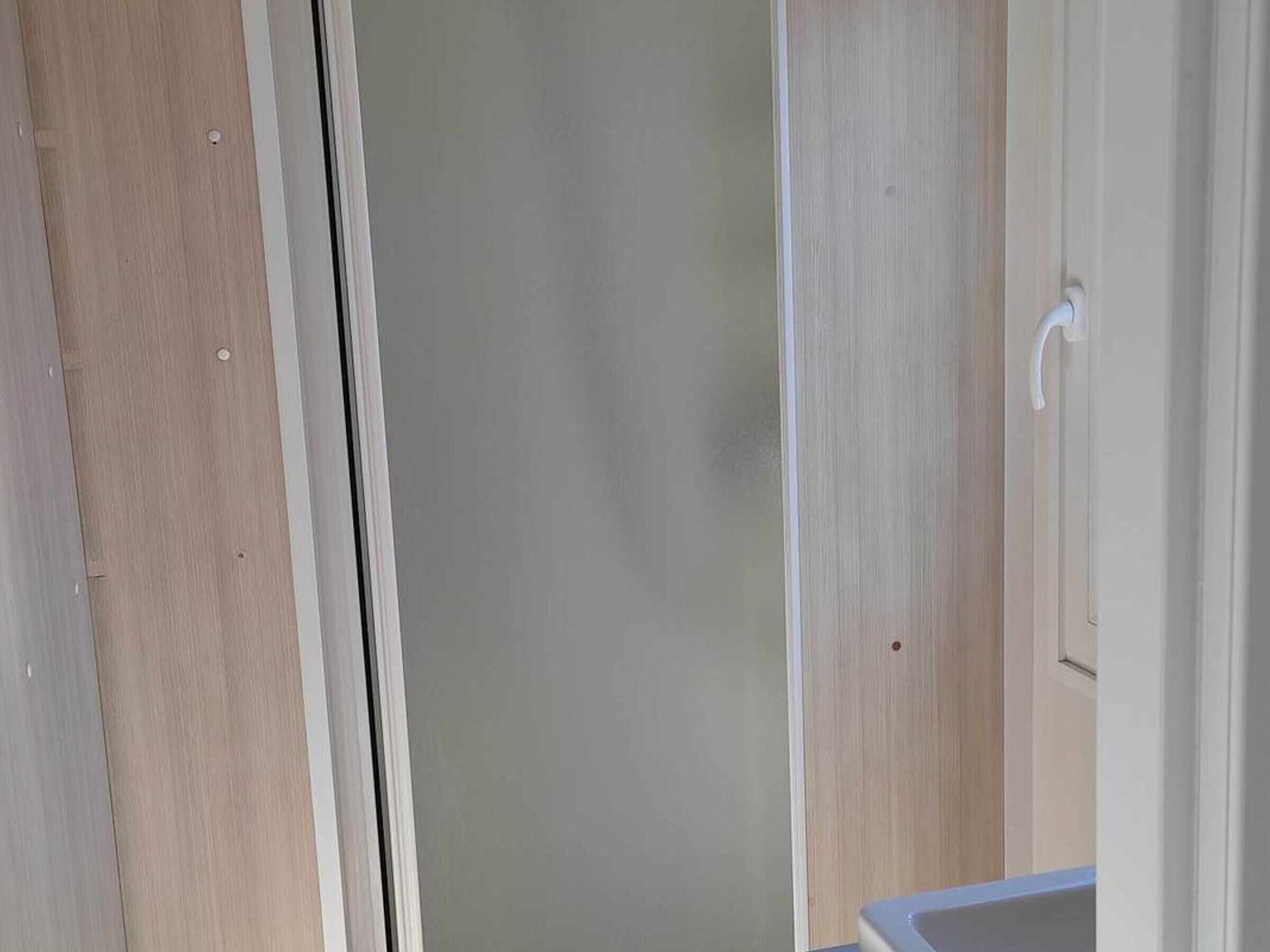 Une salle de bain avec une porte en bois, un lavabo blanc et un miroir.
