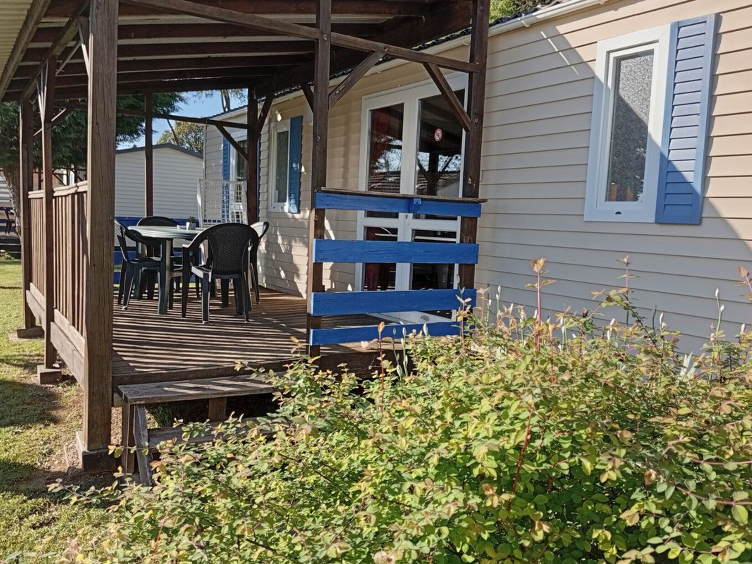 Un espacio al aire libre techado con una terraza de madera, una mesa con sillas y una cerca azul.