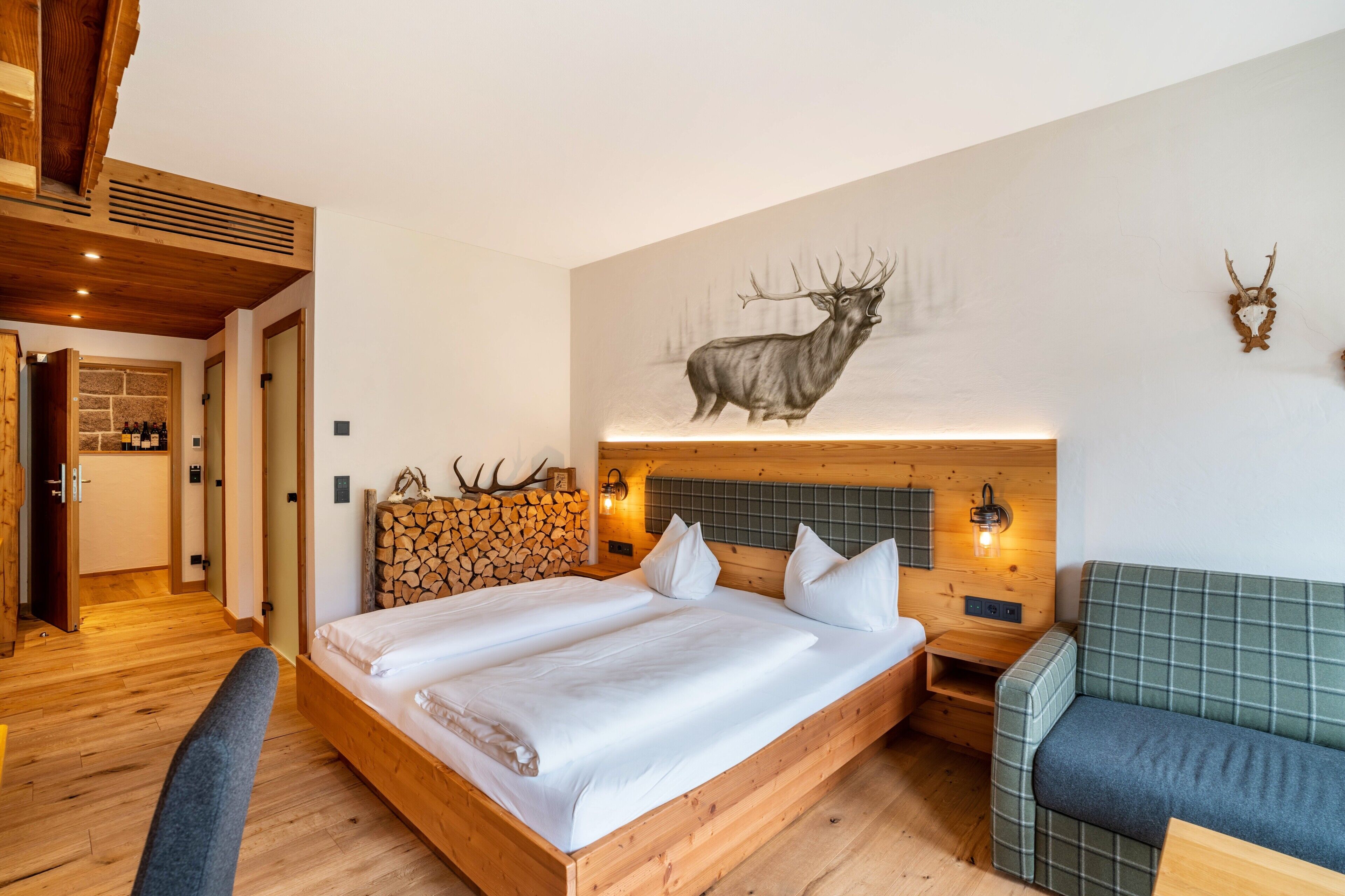 Een slaapkamer met houten vloer, een bed, een groene bank en een wanddecoratie van een hert.