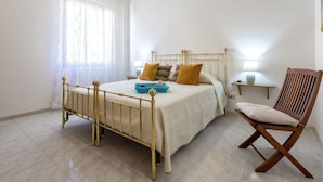 A bedroom with a bed, a chair, a bedside table, and a window with curtains. - Nice apartment for 5 guests with A/C, WIFI, TV and terrace (Alghero)