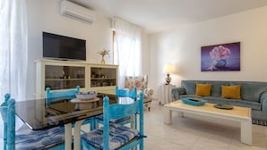 A modern living room with a glass dining table, blue chairs, a grey sofa, and a flat-screen TV. - Nice apartment for 5 guests with A/C, WIFI, TV and terrace (Alghero)