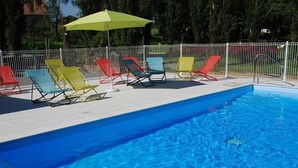 Une piscine entourée d’une clôture blanche et agrémentée de chaises longues colorées.