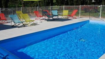 Una piscina con una cerca blanca y sillas de descanso de colores.