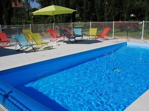 Una piscina con recinzione bianca e poltroncine da relax colorate.