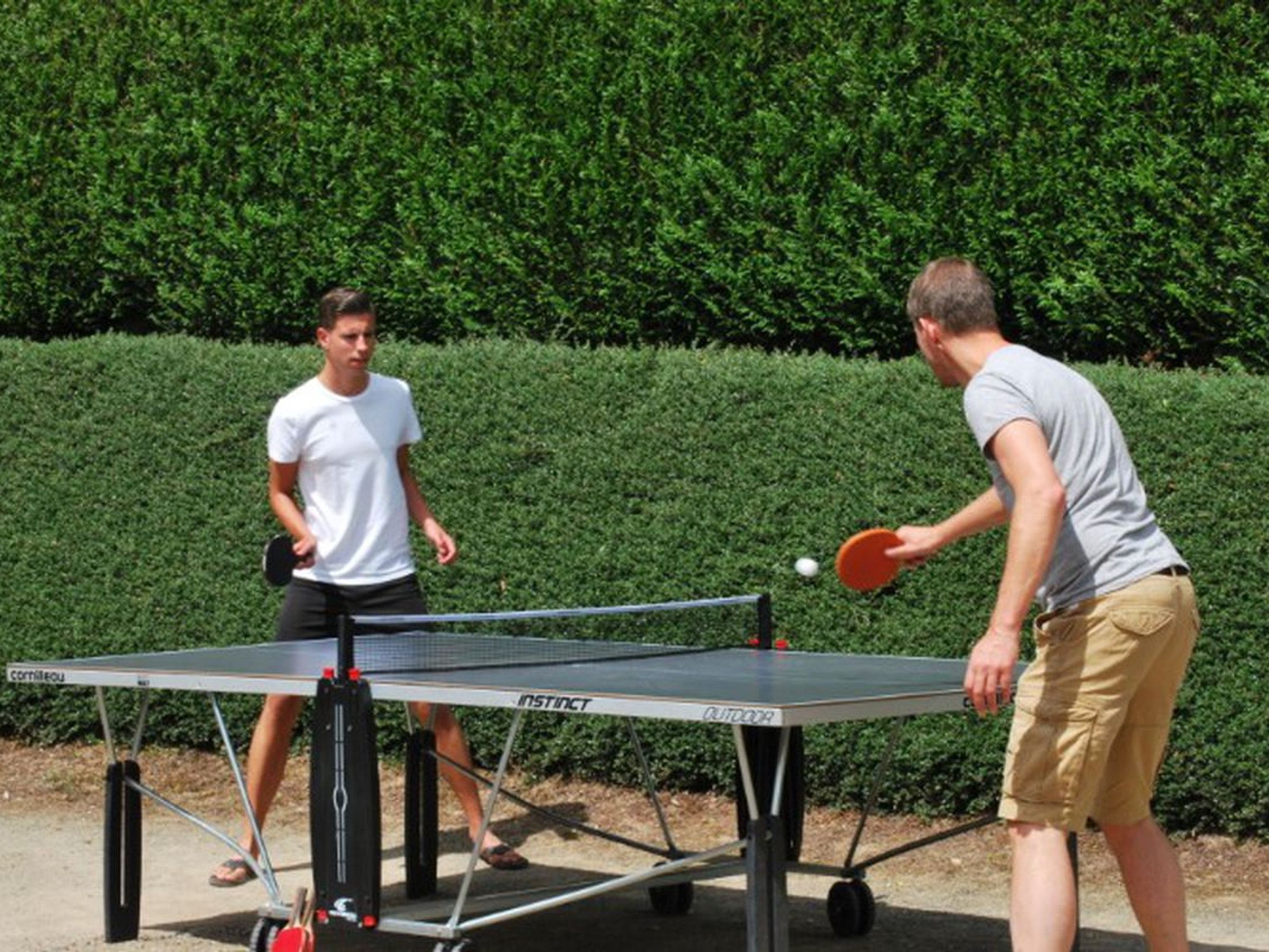 Deux personnes jouent au ping-pong à l’extérieur, sur une table portable.