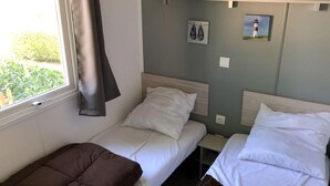 Une chambre avec deux lits simples, une fenêtre avec un rideau et une étagère fixée au mur, sur laquelle se trouvent une paire de chaussures et un tableau.