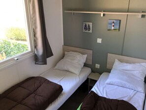 Une chambre avec deux lits simples, une fenêtre avec un rideau et une étagère fixée au mur, sur laquelle se trouvent une paire de chaussures et un tableau.