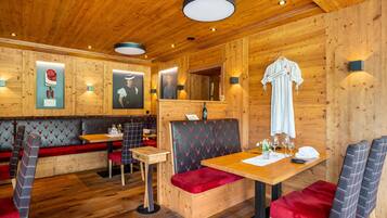 Ein Holzinnenraum mit Holzboden, einem Tisch und einer roten Sitzbank, sowie einer wandmontierten Leuchte.