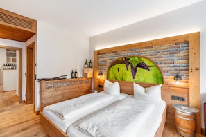 Een slaapkamer met een houten hoofdbord, een bed met wit beddengoed, een klein houten kastje met flessen en een wand met een baksteenmotief.