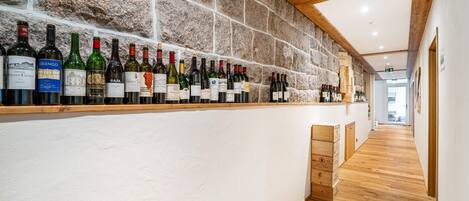 A bar area with a stone wall and wooden beams, featuring a variety of wine bottles.