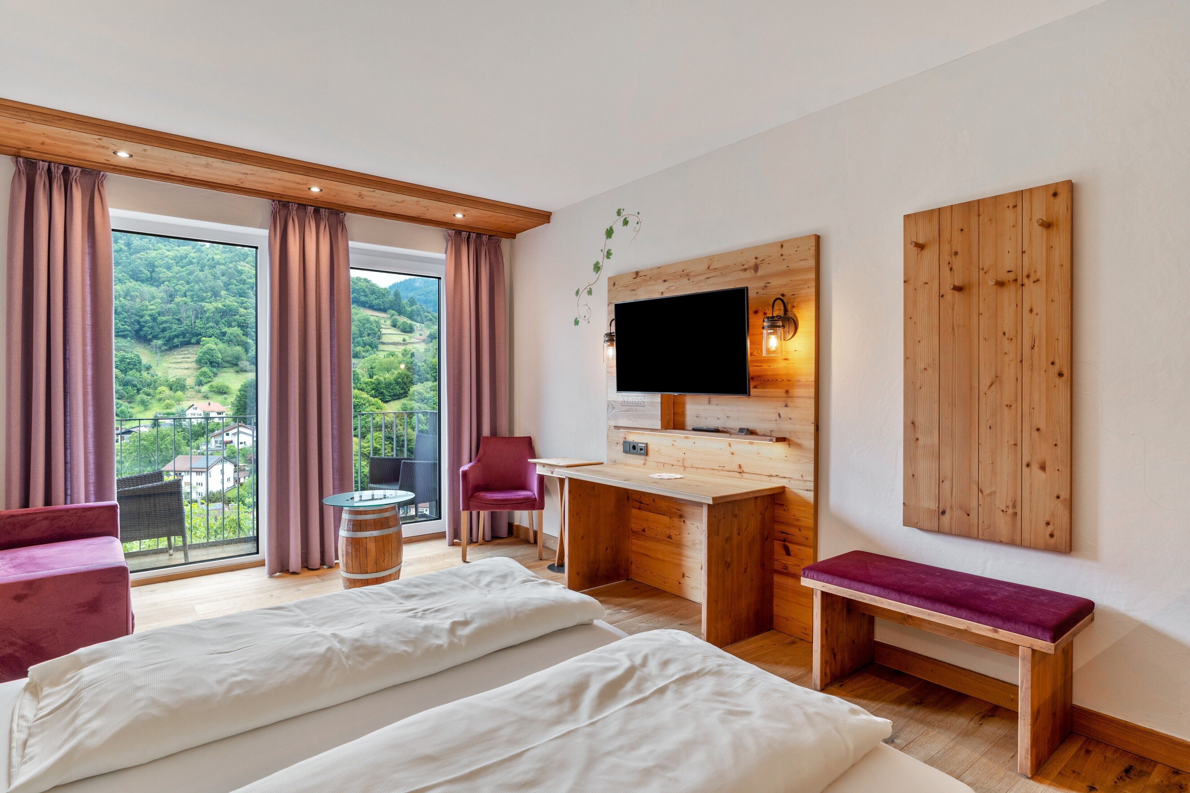 A bedroom with two beds, a desk, a chair, a TV, and a balcony with curtains.