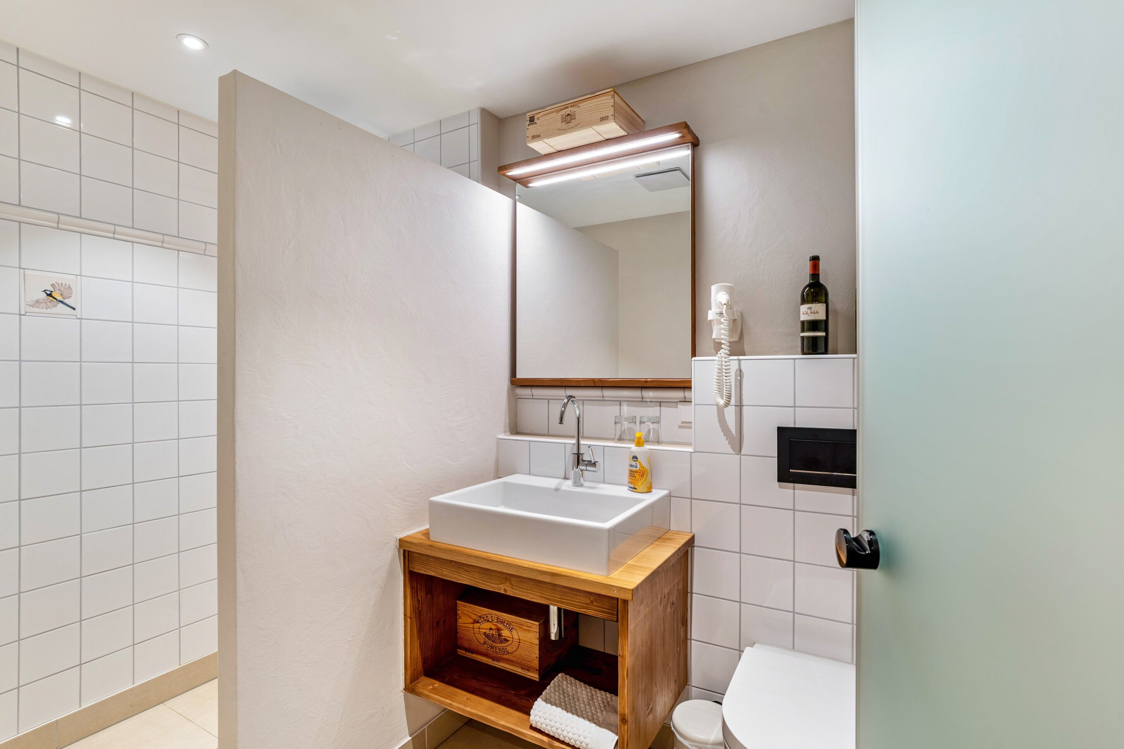 A modern bathroom with a white sink, wooden vanity, a large mirror, and a toilet.