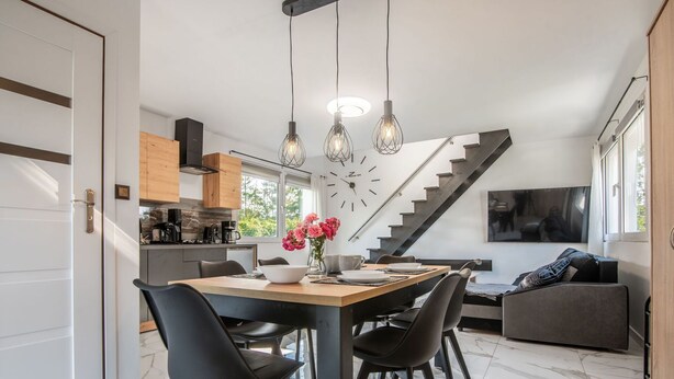Eine moderne Küche mit Essbereich, einer Treppe und einem Wohnbereich mit Sofa und Fernseher.