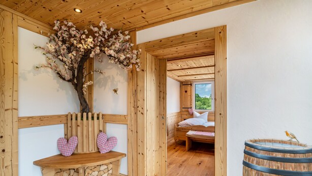 Een houten interieur met een bank, een boom met bloesems, een vat en een bed.