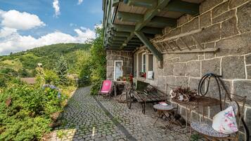 A stone building with a covered patio, outdoor seating, and a view of a green landscape.
