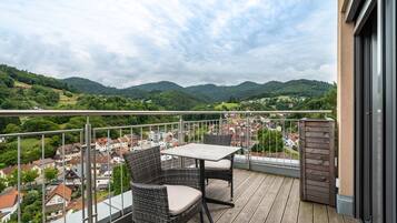 A balcony with wicker furniture, a table, and a view of a town and hills.