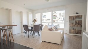 A modern living room with a sofa, dining table, chairs, and a view of the city through large windows. - Prestige Apartment & Cathedral View (Reims)