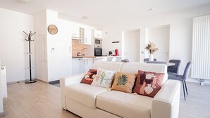 A modern living room with a beige sofa, a coat rack, and a dining area with a table and chairs. - Prestige Apartment & Cathedral View (Reims)