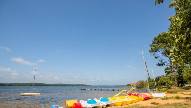 A sandy beach with colorful kayaks and a sailboat docked near the water.